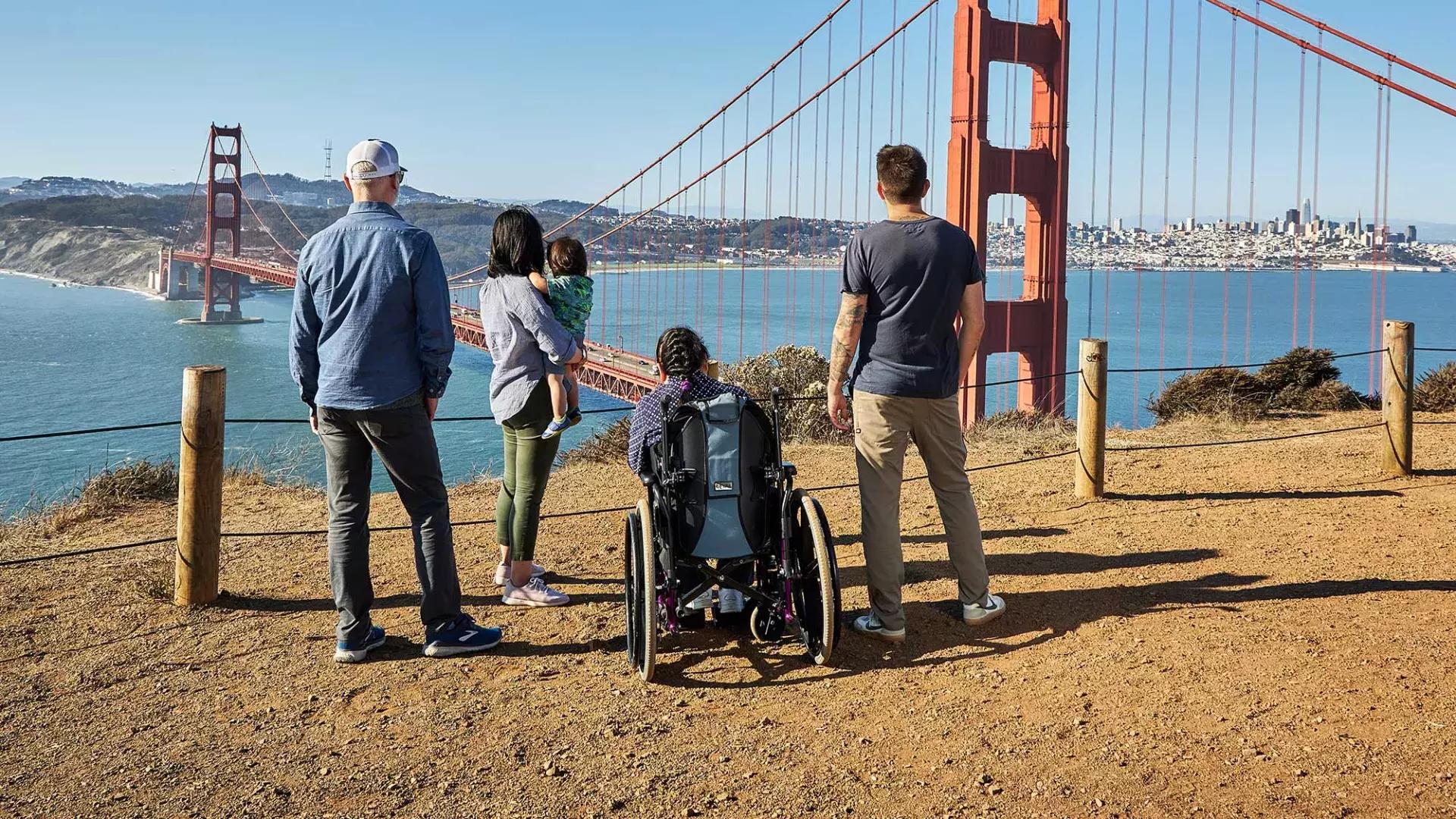 一群人, 包括一个坐轮椅的人, é visto por trás enquanto olham para a Ponte Golden Gate de Marin Headlands.