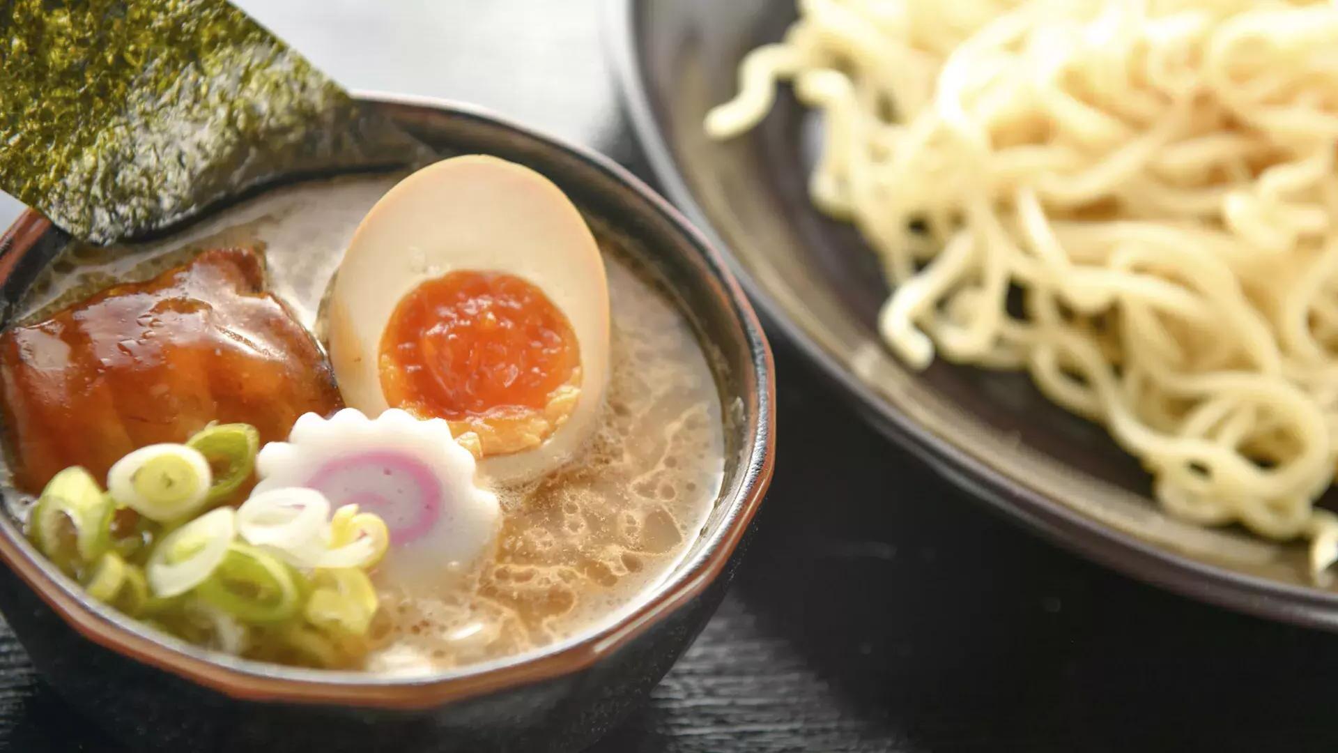 Close-up de uma tigela de macarrão e uma tigela de sopa de ramen com um ovo escalfado, 切成两半.