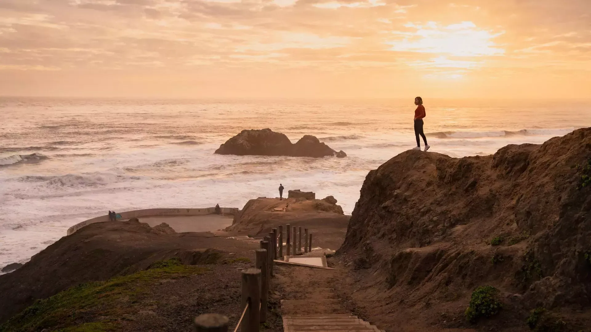 Dos personas se paran sobre rocas con vista al océano en Sutro Baths en San Francisco.