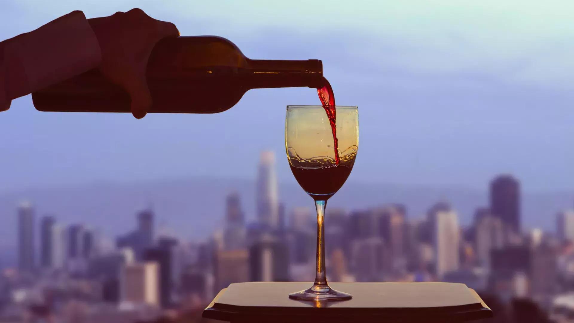 Uma taça de vinho tinto sendo servida, 和 o horizonte de 贝博体彩app visível pela janela.