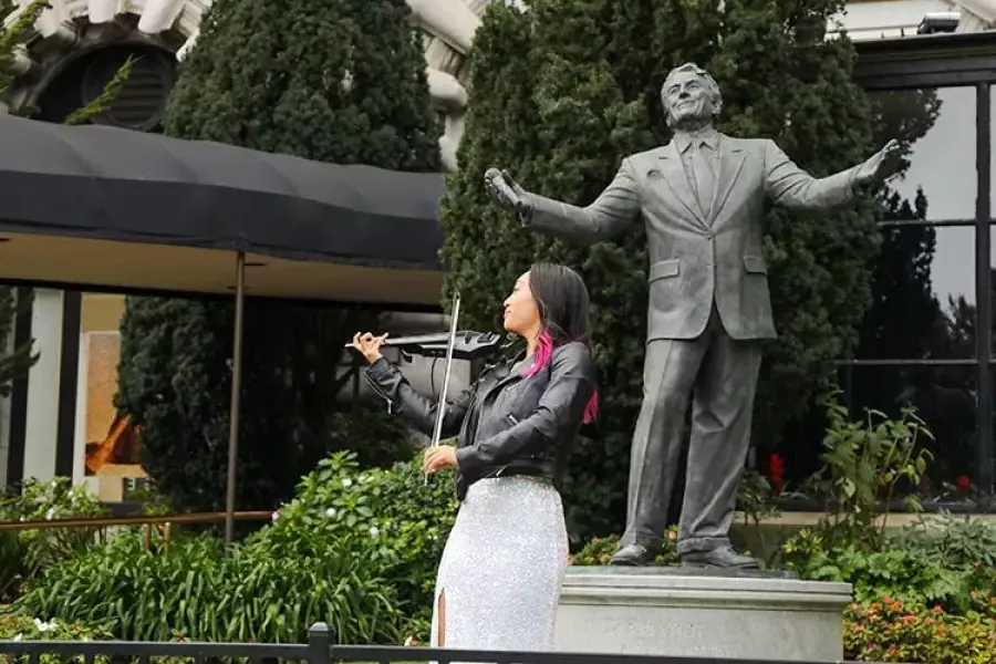 woman plays the violin in front of the Tony Bennett statue at the Fairmont Hotel.